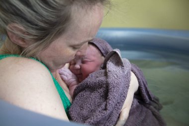 Yeni bir anne, yeni doğmuş bebeğini havuzda doğumdan sonra kucaklıyor.