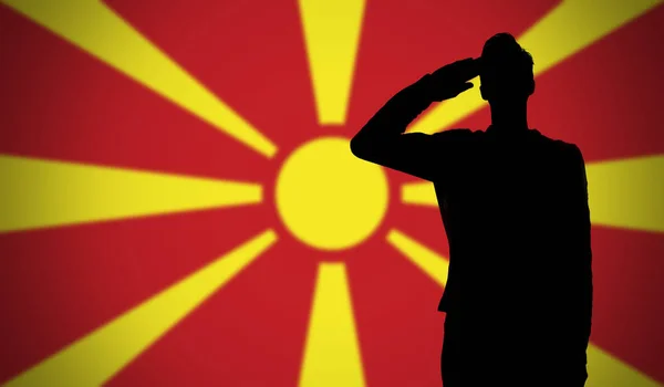 Egy katona sziluettje szalutál a macedóniai zászló előtt. — Stock Fotó