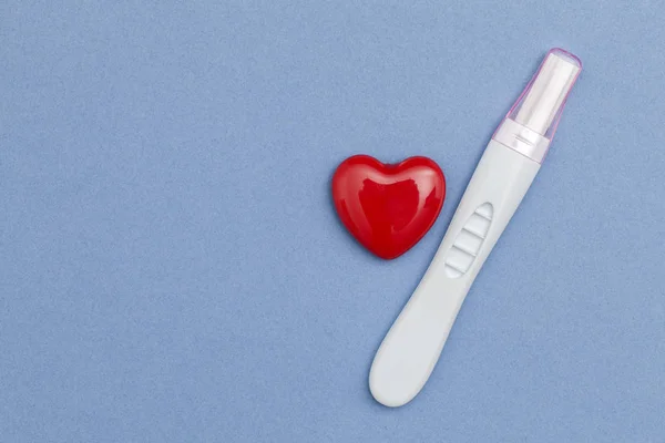 Tes kehamilan dengan hati merah pada latar belakang biru — Stok Foto