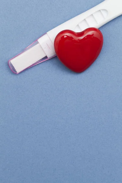 Prueba de embarazo con un corazón rojo sobre un fondo azul — Foto de Stock