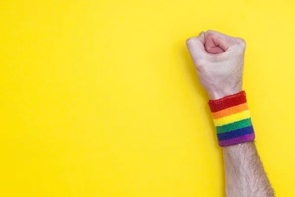 Pěst ruka s gay pýchou duha vlajka náramek na žluté zádech — Stock fotografie