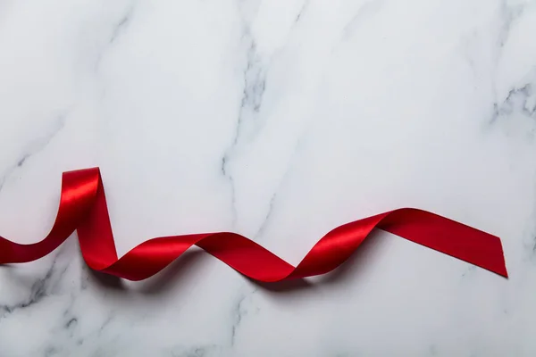 Červená saténová stuha na luxusním mramorovém pozadí — Stock fotografie
