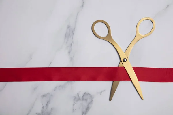Grand opening background. Gold scissors with red ribbon on a marble background