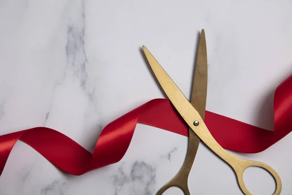 Grand opening background. Gold scissors with red ribbon on a marble background