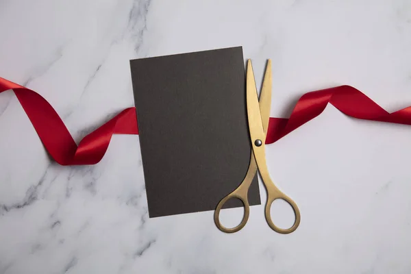 Grand opening background. Gold scissors with red ribbon on a marble background