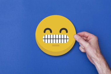 Bir emoji simgesi tutan erkek el gülümseyen kafa simgesi