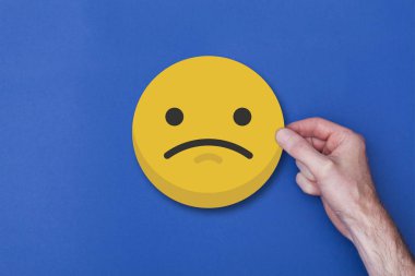 Bir emoji simgesini tutan erkek el mutsuz bir gülen kafa ikonu