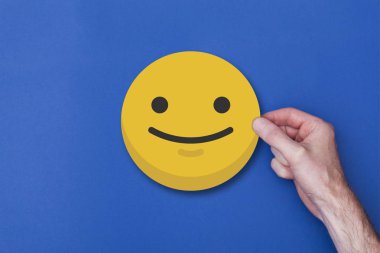 Bir emoji simgesi tutan erkek el gülümseyen kafa simgesi