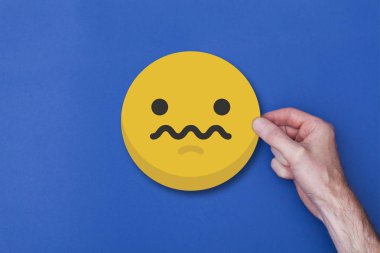 Bir emoji simgesini tutan erkek el mutsuz bir gülen kafa ikonu