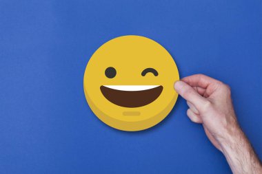 Bir emoji simgesi tutan erkek el gülümseyen kafa simgesi