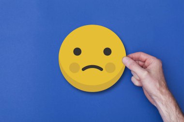 Bir emoji simgesini tutan erkek el mutsuz bir gülen kafa ikonu