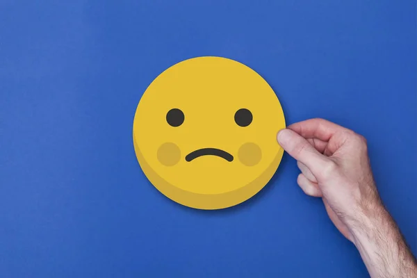 Maschio mano tenendo un emoji emoticon infelice smiley testa icona — Foto Stock