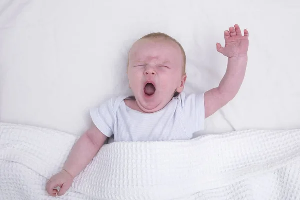 Ένα κουρασμένο μωρό κάτω από μια κουβέρτα χασμουρητό — Φωτογραφία Αρχείου