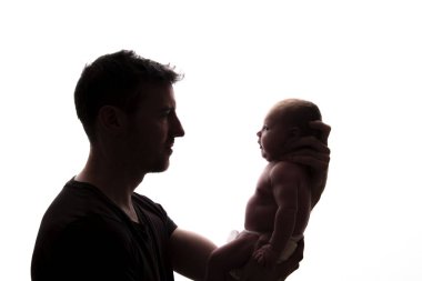 Yeni doğmuş bebeğini kucağında tutan bir babanın silüeti.