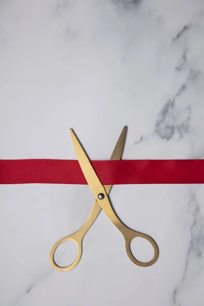 Grand opening background. Gold scissors with red ribbon on a marble background