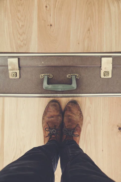 Looking down towards a persons feet and old vintage travel suitcase