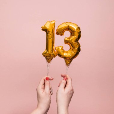 13 numaralı doğum günü kutlamasının altın balonunu tutan kadın.