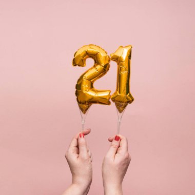 21 numaralı doğum günü kutlamasının altın balonunu tutan kadın.
