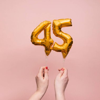 45 numaralı doğum günü kutlamasının altın balonunu tutan kadın.