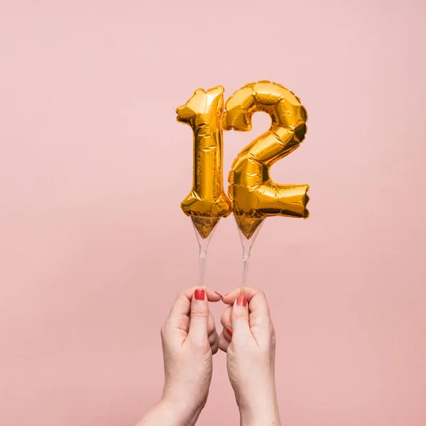 Mão feminina segurando um número 12 aniversário celebração balão de ouro — Fotografia de Stock