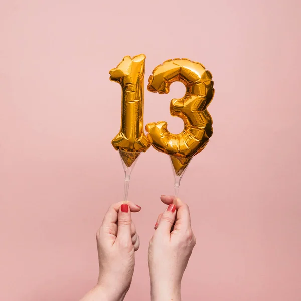 Kvinnlig hand håller en nummer 13 födelsedag firande guld ballong — Stockfoto