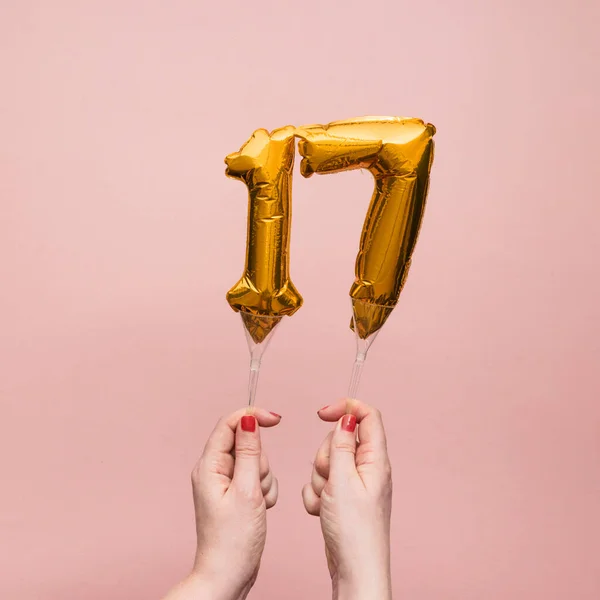 Mujer de la mano sosteniendo un número 17 aniversario celebración globo de oro — Foto de Stock