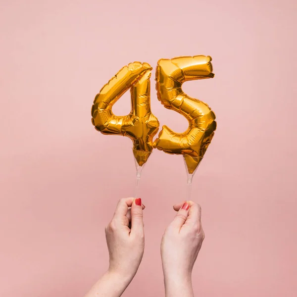 Mão feminina segurando um número 45 aniversário celebração balão de ouro — Fotografia de Stock