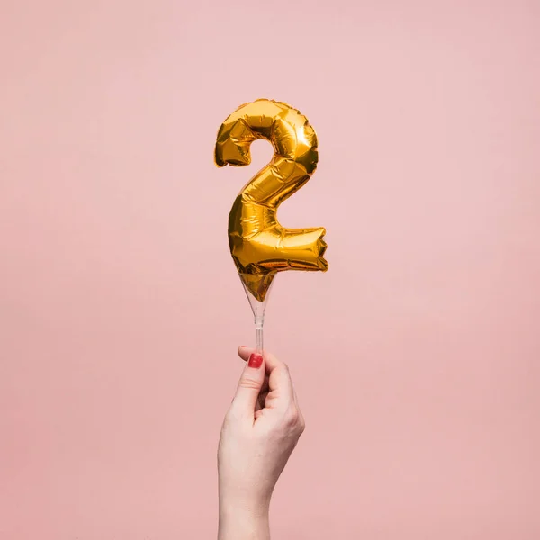Mano femminile in possesso di un numero 2 anniversario compleanno palloncino d'oro celebrazione — Foto Stock