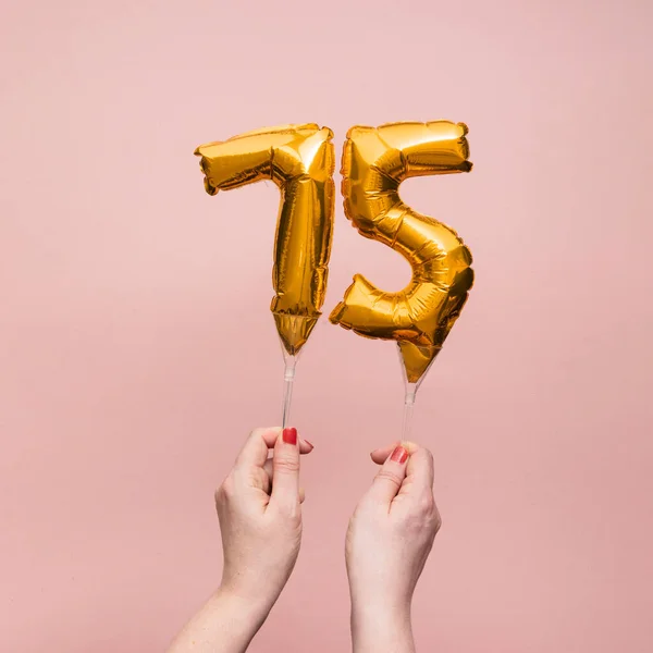 Vrouwelijke hand met een nummer 75 verjaardag viering gouden ballon — Stockfoto
