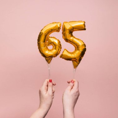 65 numaralı doğum günü kutlamasının altın balonunu tutan kadın.