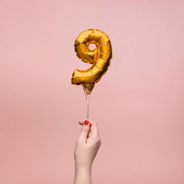 9 numaralı doğum günü kutlamasının altın balonunu tutan kadın.