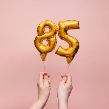 Female hand holding a number 85 birthday anniversary celebration gold balloon clipart