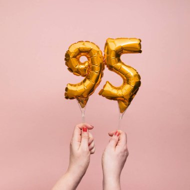 95 numaralı doğum günü kutlamasının altın balonunu tutan kadın.