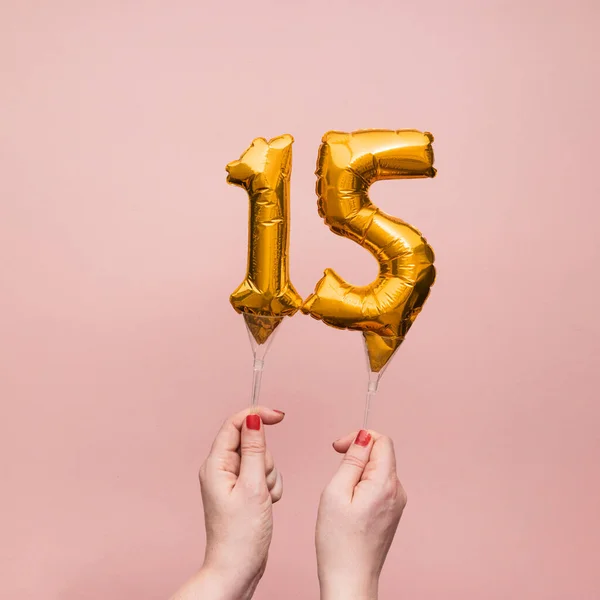 Mão feminina segurando um número 15 aniversário celebração balão de ouro — Fotografia de Stock