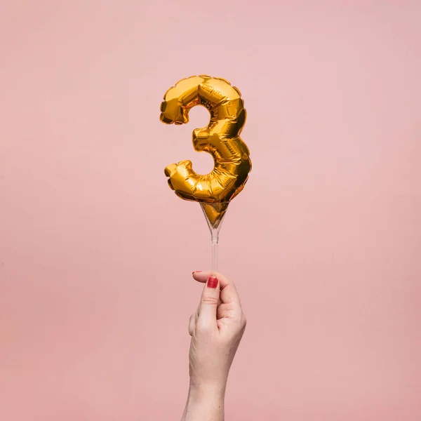 Kvinnlig hand håller en nummer 3 födelsedag firande guld ballong — Stockfoto