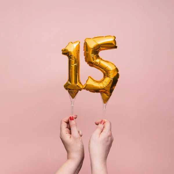 Vrouwelijke hand met een nummer 15 verjaardag viering gouden ballon — Stockfoto