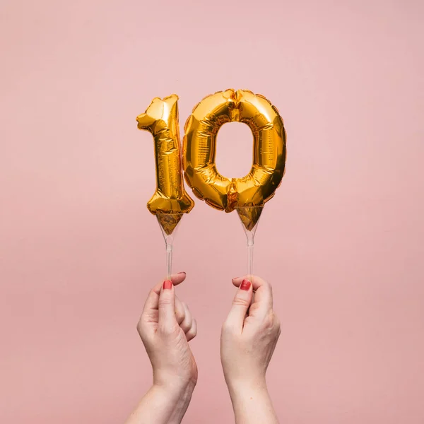 Vrouwelijke hand met een nummer 10 verjaardag viering gouden ballon — Stockfoto