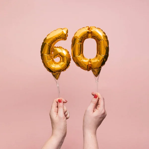 Vrouwelijke hand met een nummer 60 verjaardag viering gouden ballon — Stockfoto