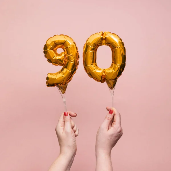 Mano femenina sosteniendo un globo de oro de celebración de aniversario número 90 —  Fotos de Stock