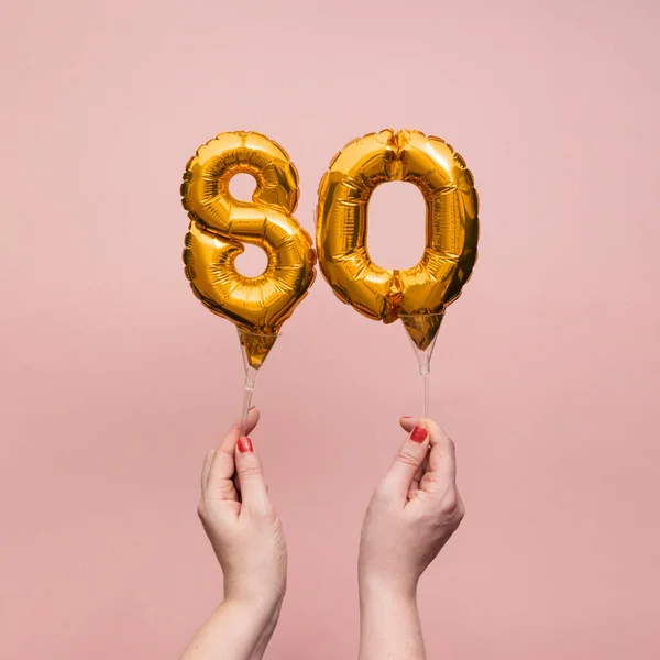 Mão feminina segurando um número 80 aniversário celebração balão de ouro — Fotografia de Stock