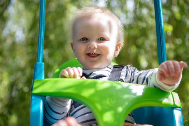 Küçük bir çocuk bahçede bir ağacın altında salıncakta sallanırken eğleniyor.