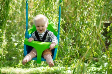 Küçük bir çocuk bahçede bir ağacın altında salıncakta sallanırken eğleniyor.
