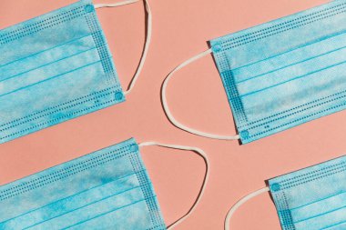 Mavi cerrahi maske pembe arka planda düz bir kompozisyon oluşturdu.