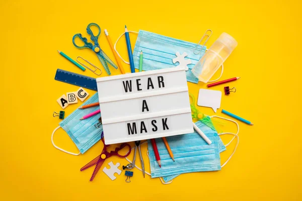 Tragen Sie eine Maske Leuchtkasten Nachricht mit Schulausrüstung und covid Masken — Stockfoto