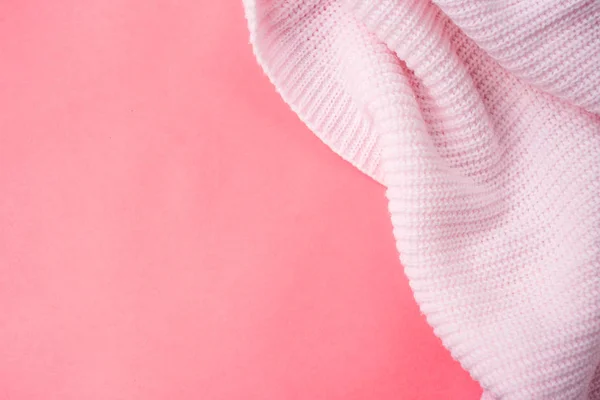 Pink knitted clothes on a pink paper background. Bedding with a pink knitted plaid. Copy space. Flat lay, top view