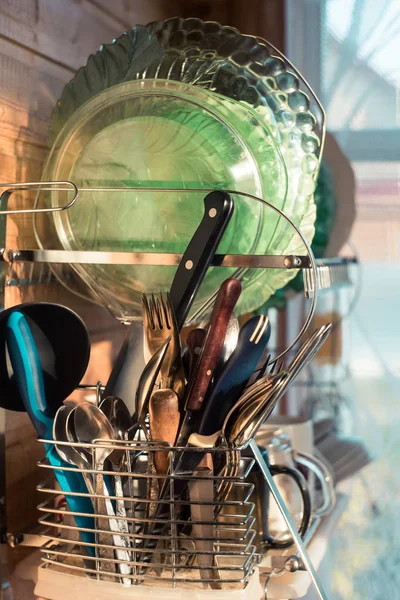 Home kitchen. Clean washed dish ware drying on a drainer mounted in kitchen. Clean dishes a spoon, plate, cup, knife, fork after washing on the shelf