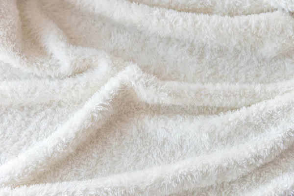 White delicate soft background of plush fabric. Texture of beige soft fleecy blanket textile with twisted folds.
