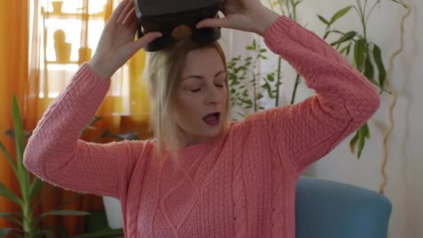 ピンクのセーターを自宅で女性を楽しんで周り現代 Armchairlooking のバーチャルリアリティのゴーグルを使用して 手でジェスチャーを使用して — ストック動画