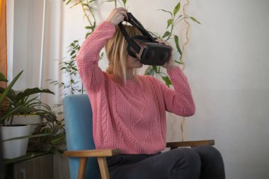 Kadın pembe kazaklı evde modern kullanarak sanal gerçeklik gözlükleri tadını koltuk etrafında arıyorsunuz ve hareketleri el ile kullanarak