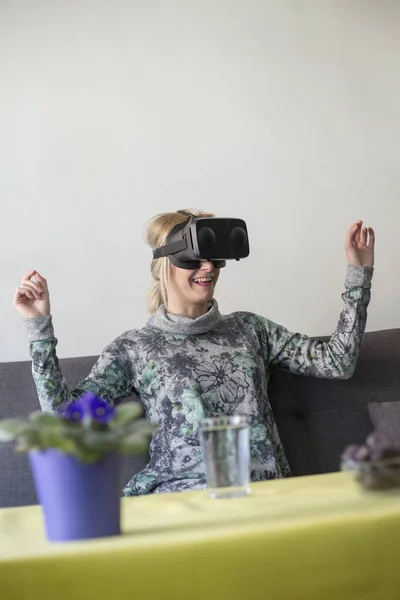 woman at home enjoying virtual reality goggles on sofa Looking around and using gestures with hands